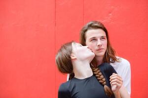 uma casal é desfrutando uma verão período de férias dentro a vermelho parede fundo, alegremente mostrando seus amor para cada outro. foto