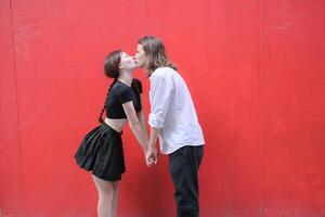 uma casal é desfrutando uma verão período de férias dentro a vermelho parede fundo, alegremente mostrando seus amor para cada outro. foto