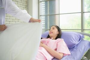 uma fêmea médico ajuda cobrir uma paciente com uma cobertor depois de chegando para Verifica e Segue acima em tratamento foto