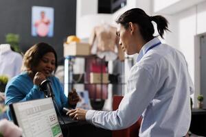 africano americano cliente pagando para casual vestir, em pé às contador escrivaninha dentro roupas loja. viciado em compras africano americano mulher compras para elegante mercadoria dentro moderno boutique foto