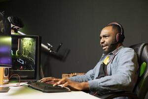 animado homem jogando intenso videogame em jogos pc às computador mesa, desfrutando dia desligado, tendo Diversão. focado jogador lutando inimigos dentro conectados multiplayer atirador, sentindo-me Forte emoções foto