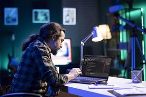 dedicada masculino programador usa dele portátil computador para gerir bases de dados e manter a olho em rede segurança. barbudo homem é codificação em uma digital computador portátil enquanto sentado às uma escrivaninha. foto