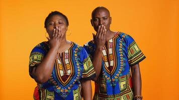 doce africano americano casal enviando ar Beijos em Câmera, apresentando provocante gesto e mostrando seus afeição. étnico homem e mulher sopro beijo dentro estúdio, tradicional roupas Unid. foto