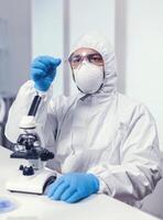 médico químico segurando microscop vidro deslizar com sangue amostra vestido dentro ppe terno dentro moderno laboratório.. examinando vacina evolução usando Alto tecnologia para pesquisando tratamento contra covid19 vírus. foto