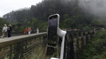 tiroteio em tripé telefone enquanto viajando. Ação. tiroteio vídeo em telefone com estabilizador enquanto viajando. tiroteio ponte com estrada de ferro dentro selva em telefone para blog foto