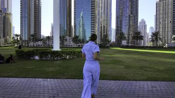 traseiro Visão do uma jovem mulher corrida em pedra caminho dentro uma cidade parque, dubai. Ação. mulher gastos Tempo ao ar livre perto alta edifícios. foto