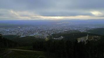 aéreo voar descida a verde montanhas para turista cidade. grampo. verão verde árvores em uma Colina declive e a cidade com nublado céu acima. foto