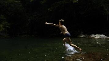 lento movimento do uma Garoto pulando para dentro uma cascata e natural lago. criativo. jovem Garoto criança tendo Diversão dentro selvas. foto