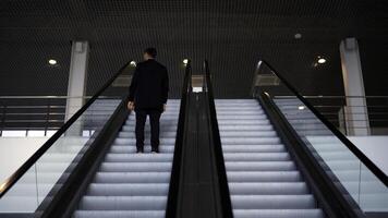 passageiro equitação em a escada rolante acima para a estação do a terra metro. meios de comunicação. traseiro Visão do uma jovem homem de negocios em a escada rolante. foto