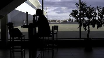 lado Visão do uma homem de negocios silhueta às a mesa às a aeroporto. meios de comunicação. trabalhando e usando computador portátil enquanto esperando para a voo. foto