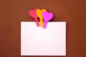 pequenos corações coloridos seguram uma nota de papel em um fundo marrom foto