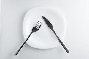 garfo e faca em um prato branco vazio sobre um fundo branco.