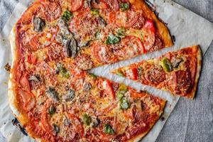 deliciosa pizza caseira com salame, tomate e cogumelos, cortada em pedaços sobre um fundo escuro de saque