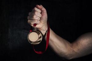 a mão de um homem sujo segura uma medalha de ouro em um fundo escuro. o conceito de sucesso foto