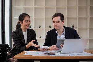 equipe o negócio do diverso parceiro o negócio mulher discutir projeto em computador portátil sentado às mesa dentro escritório. dois colega do profissional o negócio pessoas trabalhando juntos foto