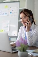 jovem ásia o negócio mulher conversa em Smartphone escrever caderno computador portátil dentro escritório. comece o negócio mulher conectados sme telemarketing foto