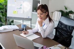 ásia o negócio mulher usando computador portátil para análise gráfico financeiro despesas relatório e planejamento para futuro dentro escritório escrivaninha foto