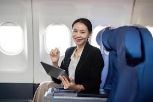 sorridente feliz o negócio mulher ásia vôo e trabalhando dentro a avião dentro primeiro aula, mulher sentado dentro a avião usando digital tábua foto
