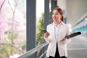 ásia o negócio mulher lindo com inteligente telefone e documento arquivo, ásia mulher com Smartphone caminhando ir para trabalhar. preparação para a trabalhando dia foto