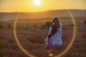 Loiras mulher poses dentro lavanda campo às pôr do sol. feliz mulher dentro branco vestir detém lavanda ramalhete. aromaterapia conceito, lavanda óleo, foto sessão dentro lavanda