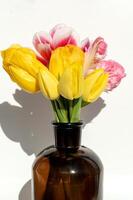 amarelo e Rosa tulipas dentro Castanho vidro garrafa em branco fundo. foto