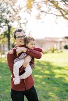 sorridente Papai abraços pequeno menina segurando dela dentro braços dentro parque foto