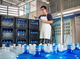 jovem ásia homem trabalhador vestem trabalhando dentro verificação engarrafado bebendo água dentro beber água fábrica antes remessa.bebendo água negócios. foto
