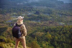 homem turista parece às a nascer do sol em a vulcão Batur em a ilha do blai dentro Indonésia. caminhante homem com mochila viagem em topo vulcão, viagem conceito foto