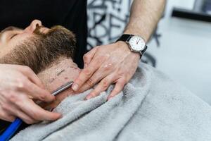 barbear processo do barbas dentro barbearia. fechar acima tiro do barbeiro faz uma corte de cabelo barba cliente com em linha reta navalha. foto