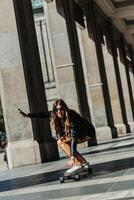 lindo jovem skatista mulher equitação em dela Longboard dentro a cidade. à moda menina dentro rua roupas passeios em uma Longboard. foto