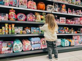 budva, Montenegro - 18 agosto 2023. pequeno menina carrinhos dentro frente do a prateleiras com brinquedos dentro a supermercado foto