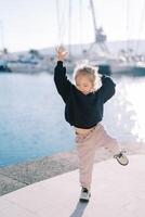 pequeno menina dançando acenando dela braços e pernas em a aterro foto