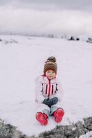 pequeno menina sentado em uma Nevado pasto foto