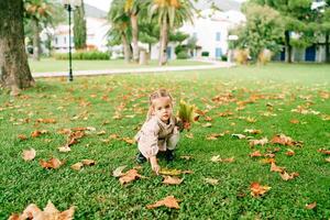 pequeno menina coleta uma ramalhete do amarelo folhas agachado em a gramado perto a casa foto