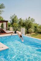 jovem homem mergulhos com dele braços frente para dentro a piscina perto a Sol espreguiçadeiras foto