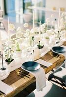 Preto pratos ficar de pé em uma de madeira mesa perto branco buquês do flores e velas em uma limitar toalha de mesa foto