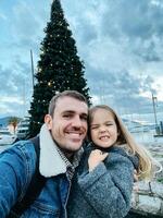 sorridente Papai com pequeno menina perto decorado Natal árvore em cais foto