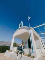 afins, Grécia - 20 agosto 2023. menina dentro oculos de sol senta em a passos do uma pequeno Igreja de a mar foto