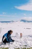 Papai e pequeno menina faço uma boneco de neve enquanto sentado dentro a neve dentro uma compensação foto