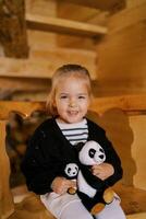 pequeno sorridente menina sentado com suave brinquedo pandas em uma de madeira cadeira foto