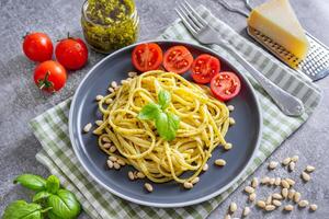 tradicional italiano espaguete massa pesto com fresco manjericão folhas e ingredientes em cinzento fundo foto