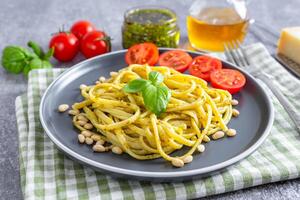 tradicional italiano espaguete massa pesto com tomate e fresco manjericão folhas dentro Preto tigela foto