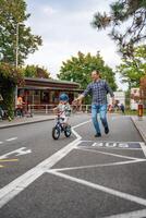 Praga, tcheco república - Outubro 10, 2023. feliz jovem pai ensina criança filha para passeio público bicicleta em tráfego Parque infantil dentro Praga, tcheco república, Europa. Alto qualidade foto