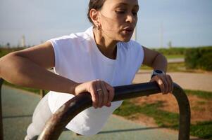 desportivo jovem mulher dentro roupa de esporte fazendo Barra flexões, exercício ao ar livre dentro a urbano quadra esportiva foto