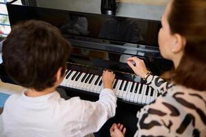 Visão a partir de acima do a adorável adolescente Garoto desfrutando jogando grande piano às lar, criando música e canção, realizando trilha sonora em a piano, composição uma melodia durante música lição. foto