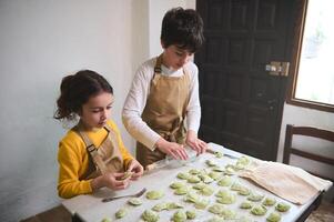 adorável crianças dentro a rural cozinha, rolando Fora massa com uma vinho garrafa, escultura dumplings com amassado batatas enchimento. cozinhando caseiro vegetariano dumplings, italiano Ravioli ou ucraniano Varenyky foto