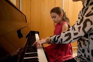 pequeno menina tendo uma piano lição com dela professor às lar. pequeno criança menina colocando dela dedos em Preto e branco chaves, criando a ritmo do música, composição melodia e cantando Natal música foto