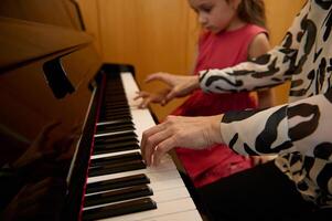 fechar-se mulher pianista segurando mãos em piano teclado, tocante Preto e branco chaves, pré-formando clássico melodia durante enquanto dando uma música lição para dela pequeno aluna garota. foto