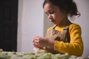 pequeno menina estofamento e moldagem bolinho de massa dentro a casa cozinha foto