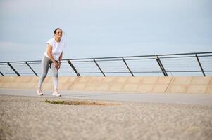 cheio comprimento tiro do a Exausta jovem mulher dentro roupa de esporte corrida em a cidade ponte estrada foto